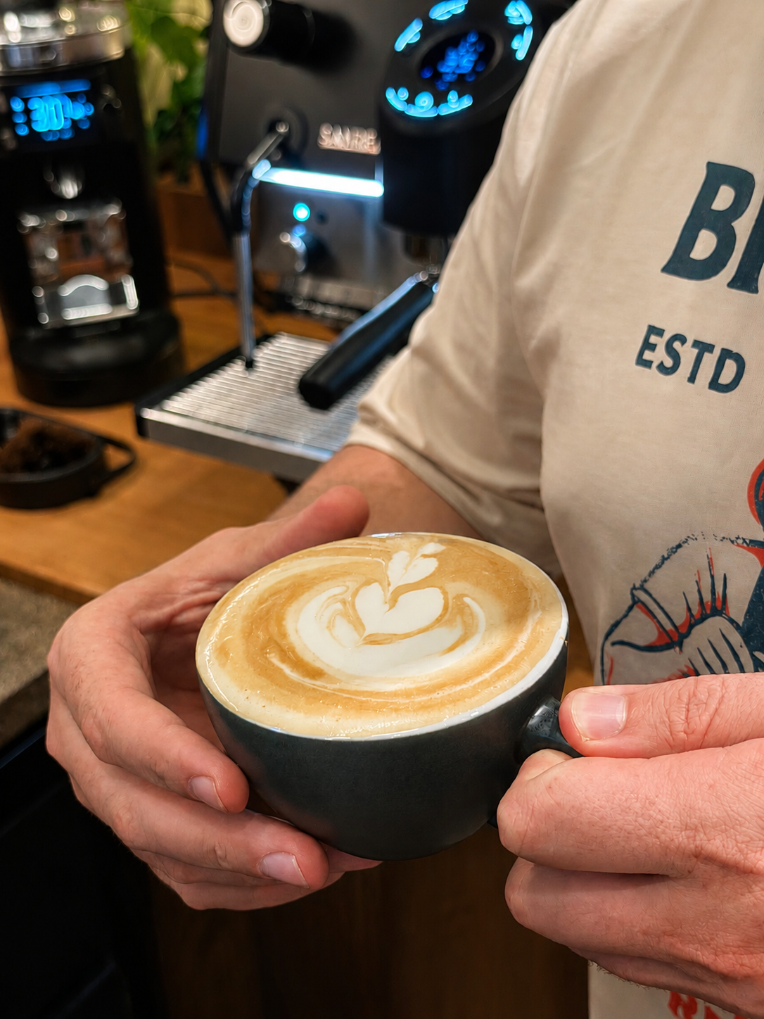 Café com leite com latte art servido nas mãos de um barista